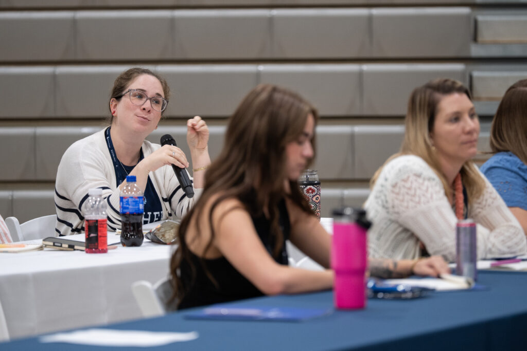 An attendee speaks into a handheld microphone while other educators listen.