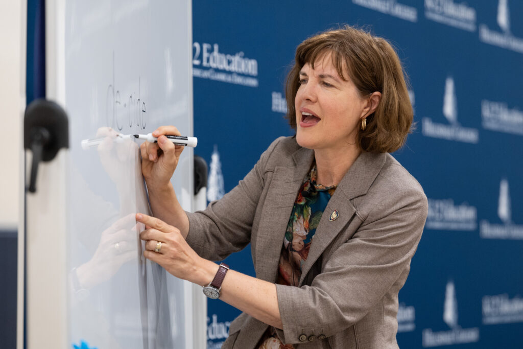 A seminar presenter writes on a whiteboard while demonstrating a classroom lesson.