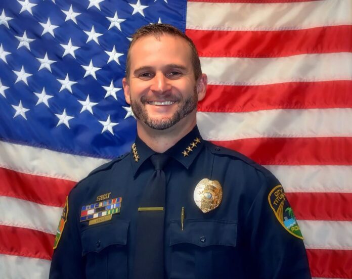 Titusville Police Chief Tyler 'TJ' Wright in uniform standing in front of an American flag